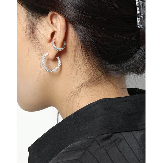 Earcuff argenté minimaliste sans perçage associé à une boucle d'oreille créole brillante.