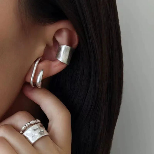 Détail d'une manchette d'oreille vintage argentée accompagnée de bagues martelées assorties.