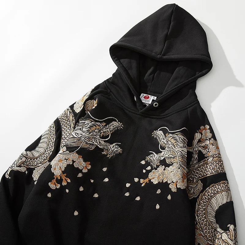 Zoom sur le buste du sweat noir montrant la finesse des broderies de dragons et des pétales blancs.