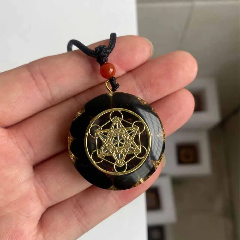 Collier orgonite rond en pierre naturelle noire avec motif géométrie sacrée doré tenu dans une main