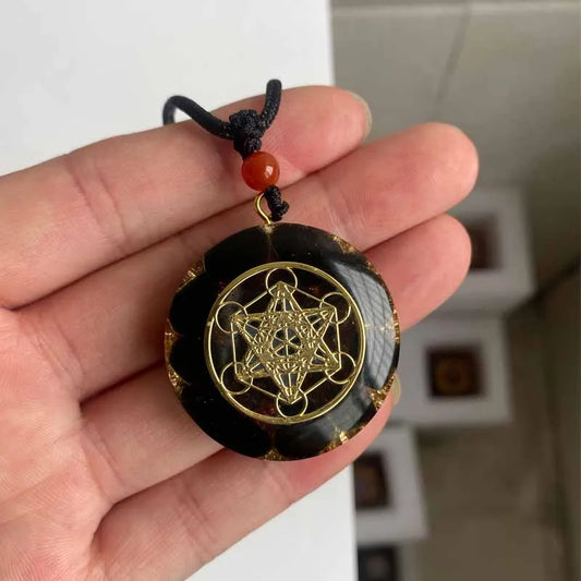 Collier orgonite rond en pierre naturelle noire avec motif géométrie sacrée doré tenu dans une main
