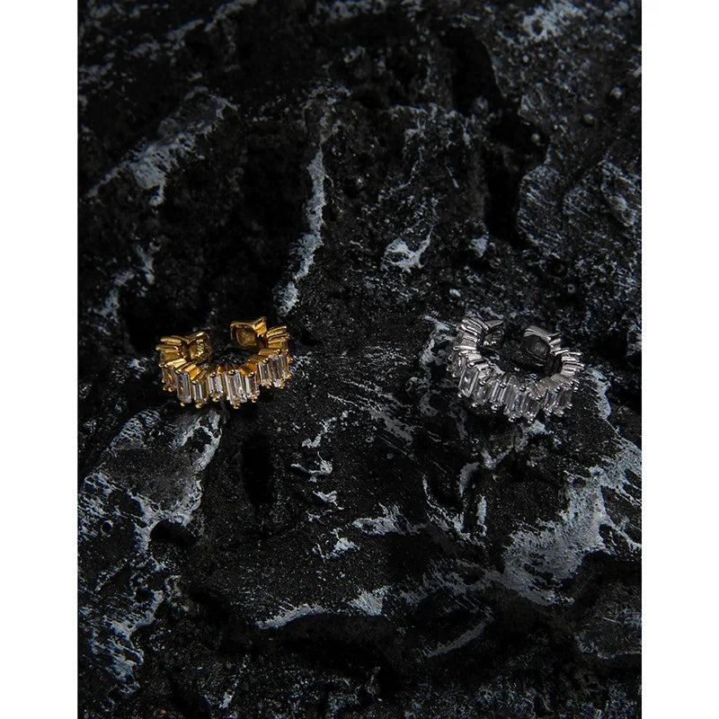 Détail des bagues d'oreilles sans perçage en argent et or posées sur une roche volcanique texturée.