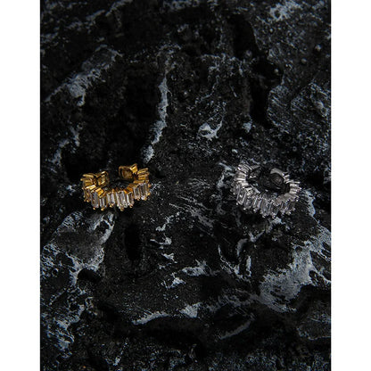 Détail des bagues d'oreilles sans perçage en argent et or posées sur une roche volcanique texturée.