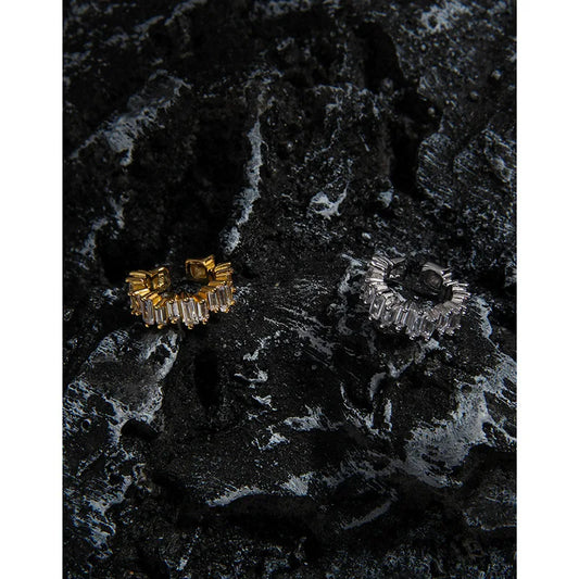 Détail des bagues d'oreilles sans perçage en argent et or posées sur une roche volcanique texturée.
