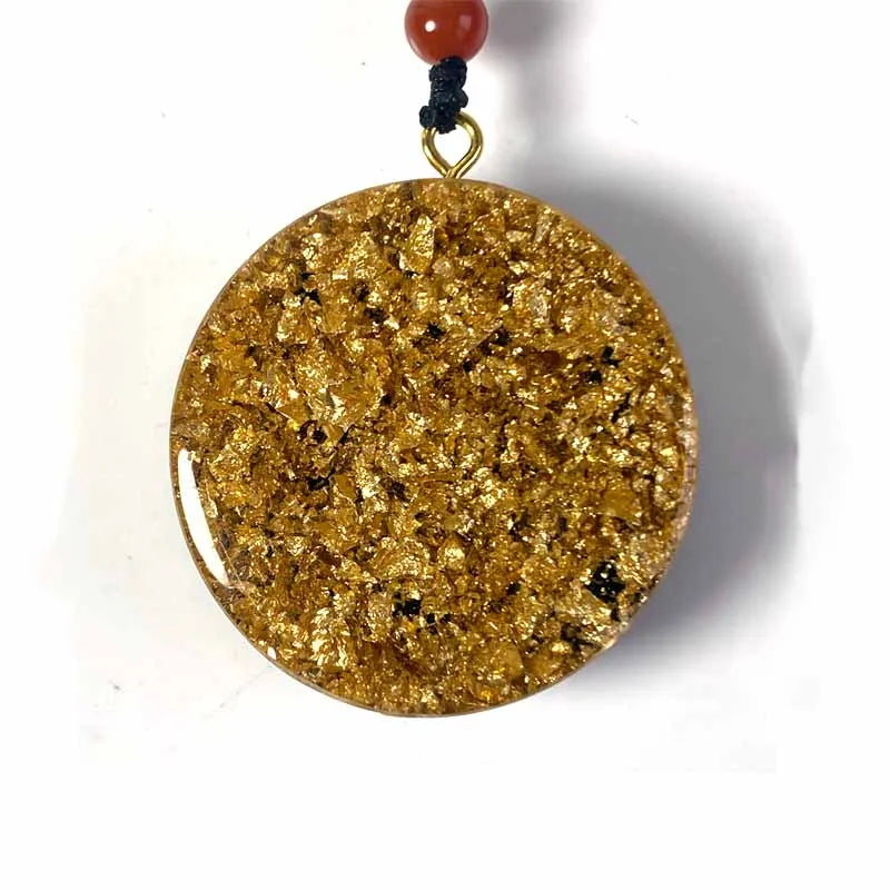 Vue de face du pendentif orgonite circulaire aux éclats de feuilles d'or scintillantes sous résine.