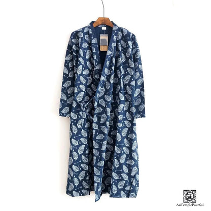 Kimono bleu marine décoré d'un motif feuillage blanc, affichant une esthétique naturelle et relaxante. Accroché sur un cintre en bois, il apporte une touche de sérénité et de style à la garde-robe contemporaine.