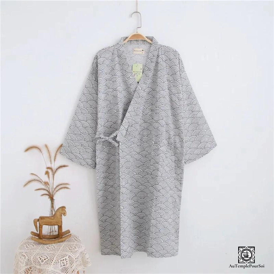 Kimono gracieux présentant un motif Seigaiha gris traditionnel, suspendu dans un cadre rustique avec des touches décoratives naturelles, capturant l'essence de la simplicité et de l'élégance japonaise.