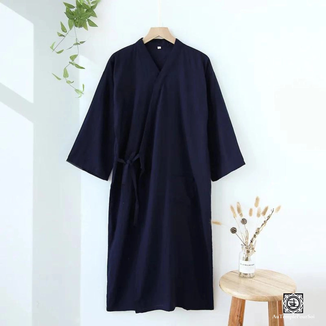 Kimono bleu nuit affichant une élégance simple, suspendu dans un espace lumineux aux accents naturels, symbolisant le confort et la sobriété du style japonais moderne.