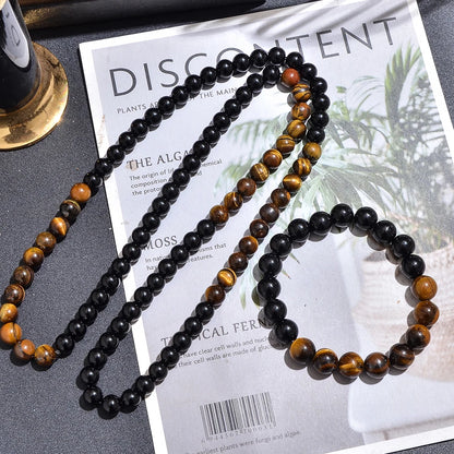 Ensemble collier long et bracelet en perles d'œil de tigre et onyx noir sur un magazine.