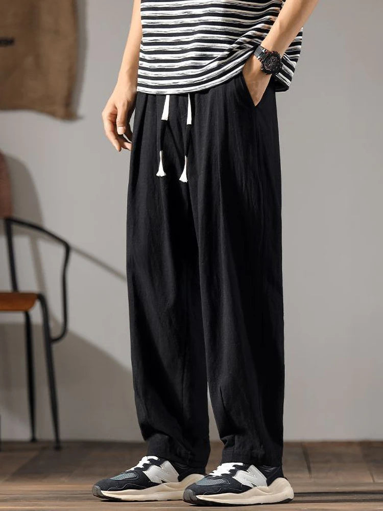 Pantalon noir en coton et lin, vue de face avec cordon de serrage à pompons blancs et poches latérales.