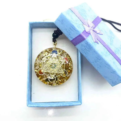 Pendentif énergétique arbre de vie posé près de sa boîte avec ruban satiné bleu.