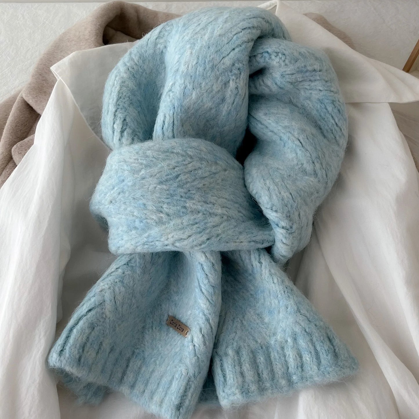 Écharpe en laine tricotée bleu ciel nouée sur une chemise blanche, vue rapprochée de la maille douce.