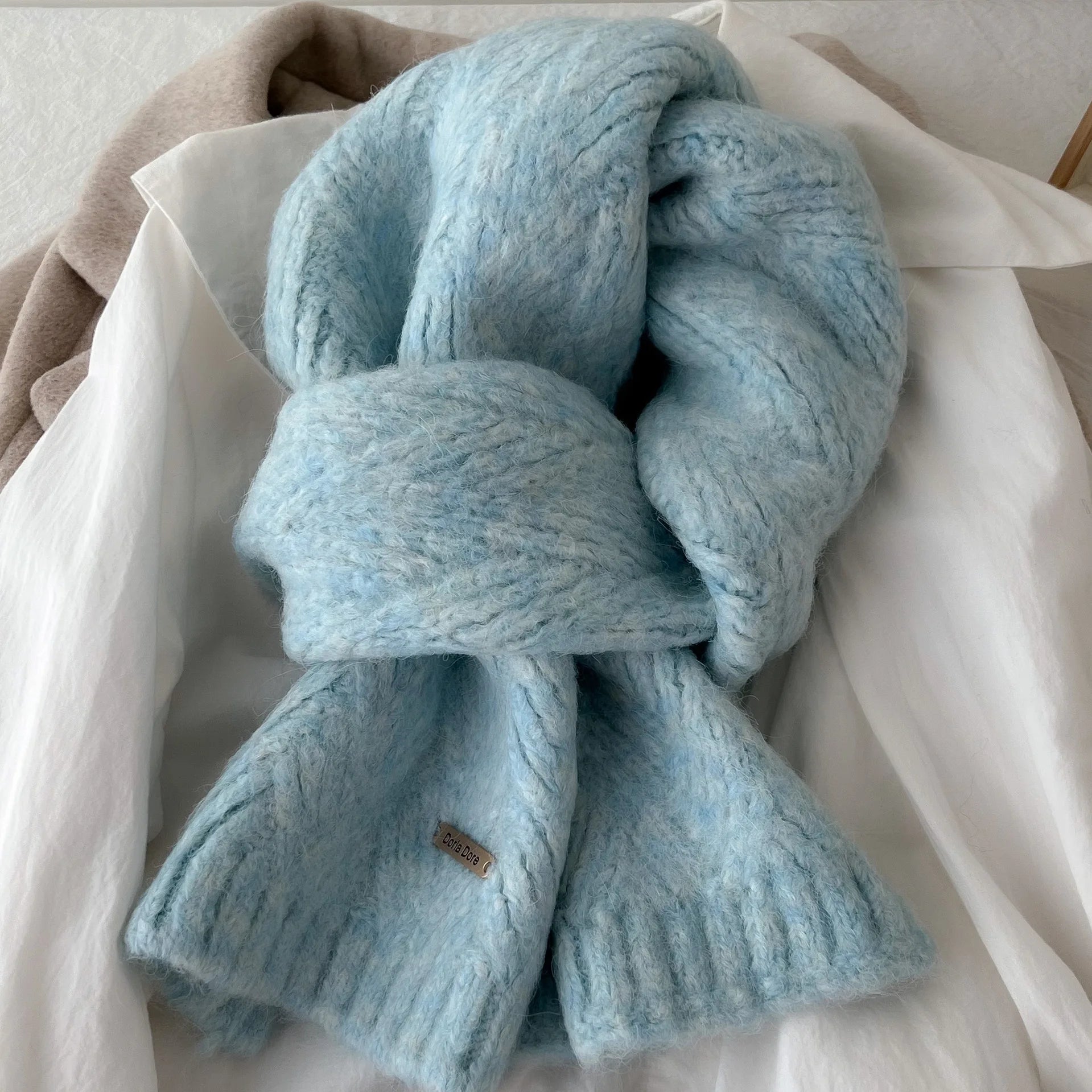 Écharpe en laine tricotée bleu ciel nouée sur une chemise blanche, vue rapprochée de la maille douce.