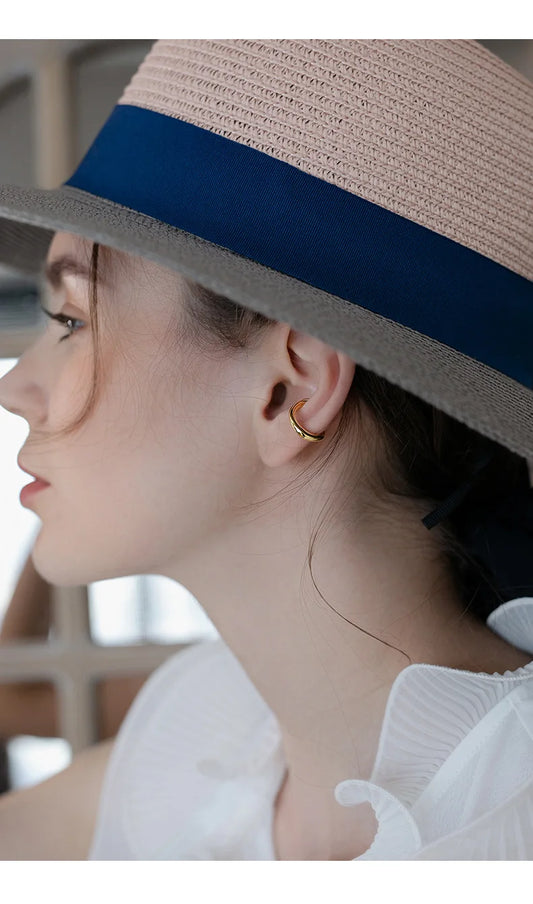 Earcuff doré en argent massif porté sur le cartilage de l'oreille d'une femme avec un chapeau