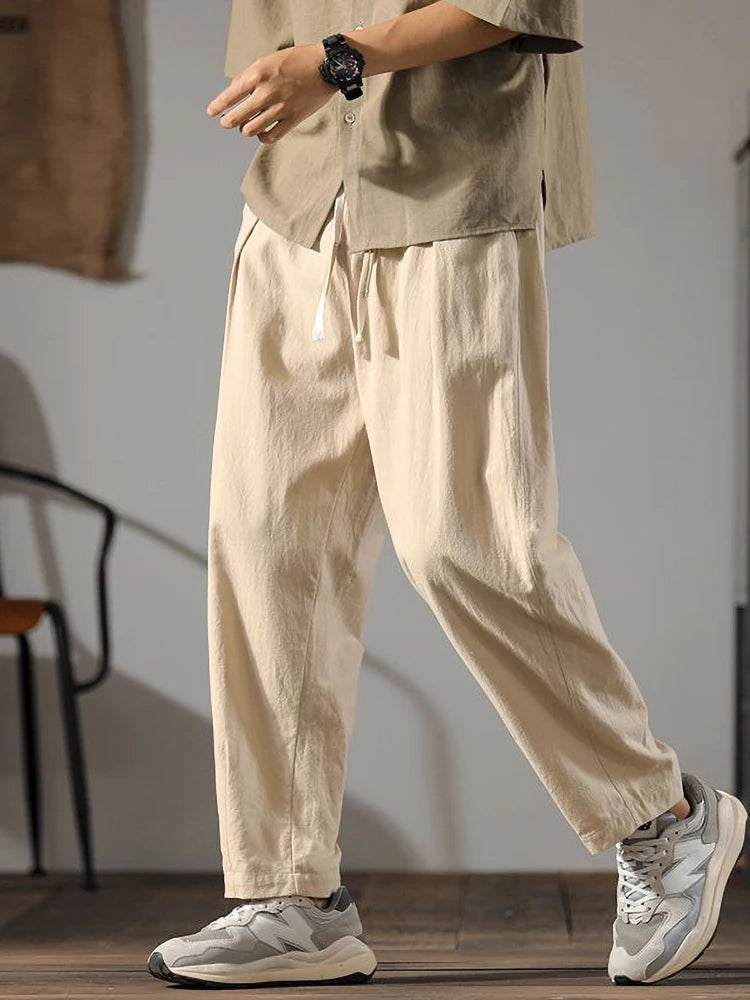 Pantalon ample en lin et coton couleur kaki, coupe droite et taille élastique, porté avec des baskets.