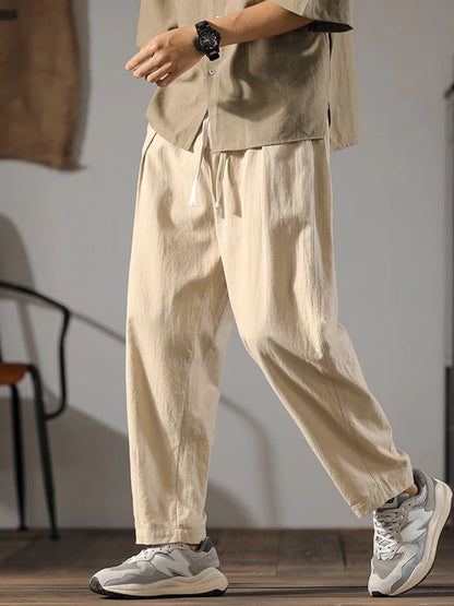 Pantalon ample en lin et coton couleur kaki, coupe droite et taille élastique, porté avec des baskets.