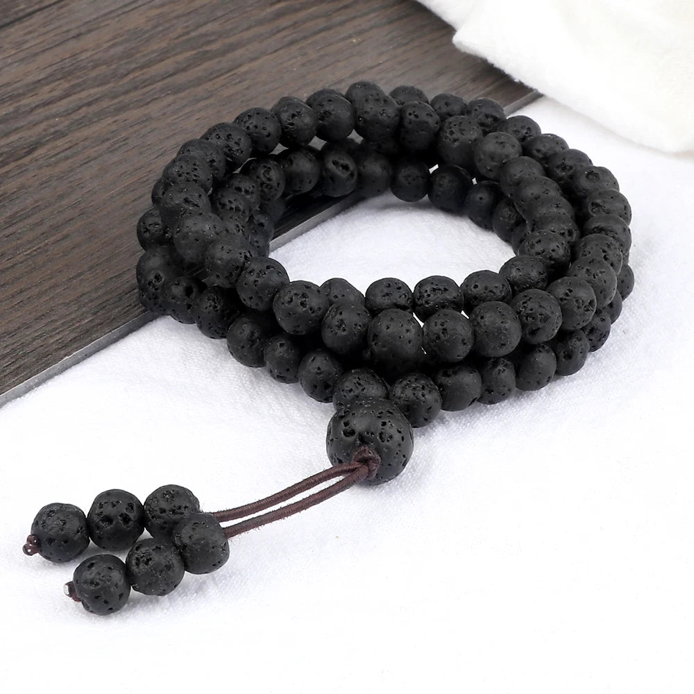 Mala en pierre de lave noire poreuse, enroulé en bracelet sur un support bicolore bois et blanc.