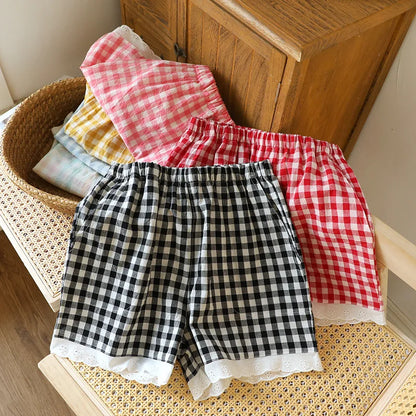 Short de pyjama en gaze de coton vichy noir, rouge et rose empilés sur une chaise en rotin