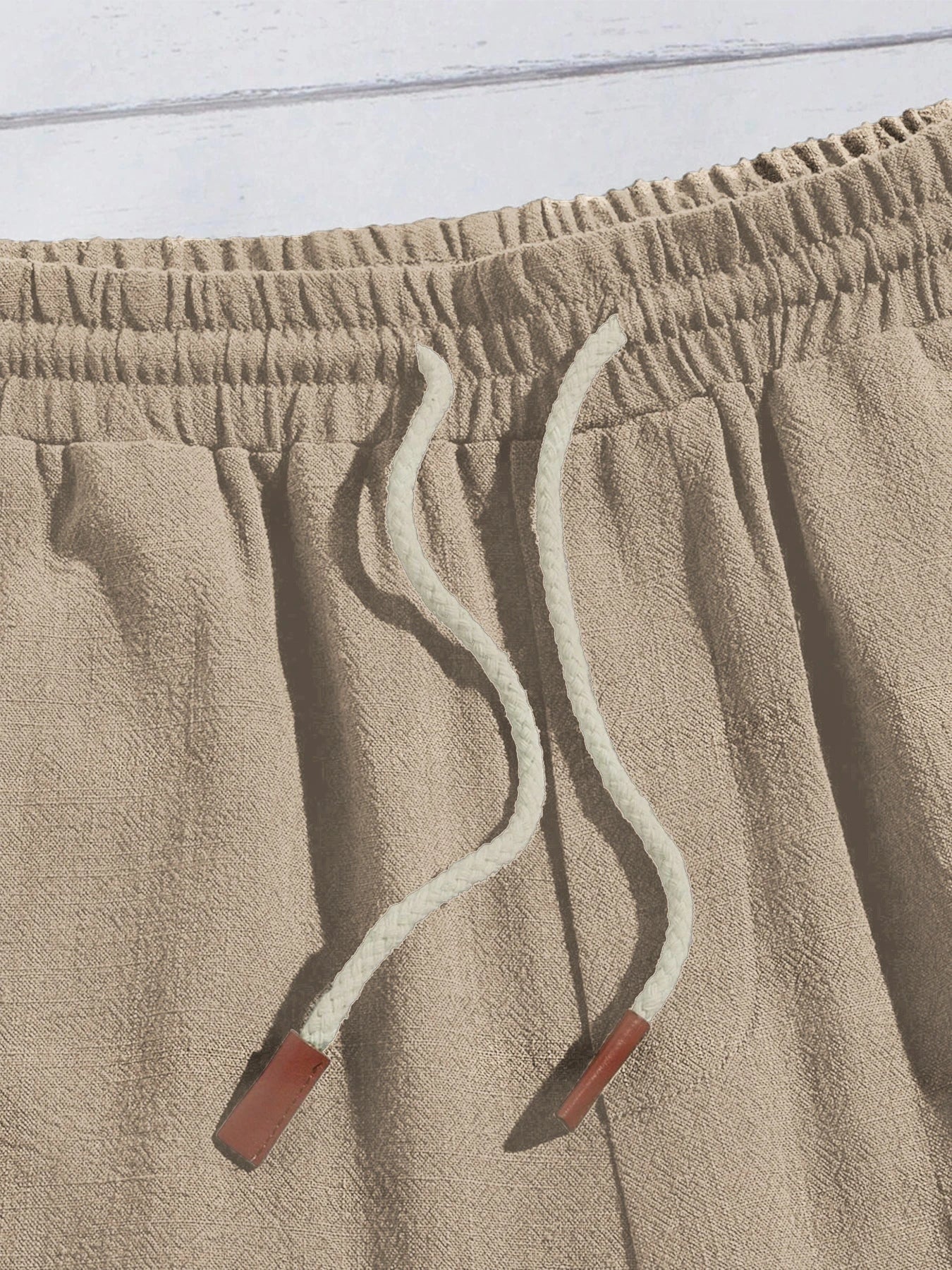 Détail du cordon de serrage blanc avec embouts marron sur le short beige.