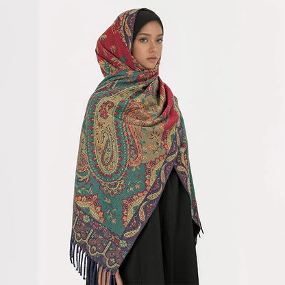 Femme portant le châle jacquard vert et rouge sur la tête, soulignant les motifs paisley et les franges bleues.