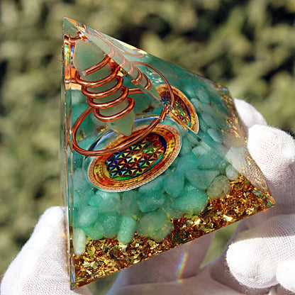 Vue rapprochée d'une pyramide énergétique tenue à la main, révélant ses couches de pierres et feuilles d'or.