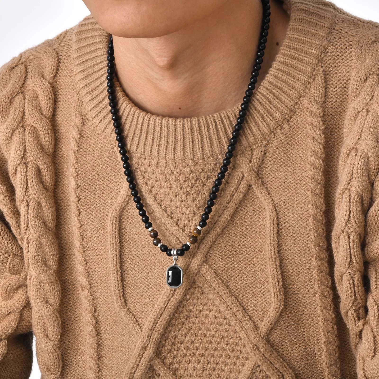 Collier de perles noires et œil de tigre porté par un homme sur un pull en maille beige, style zen.