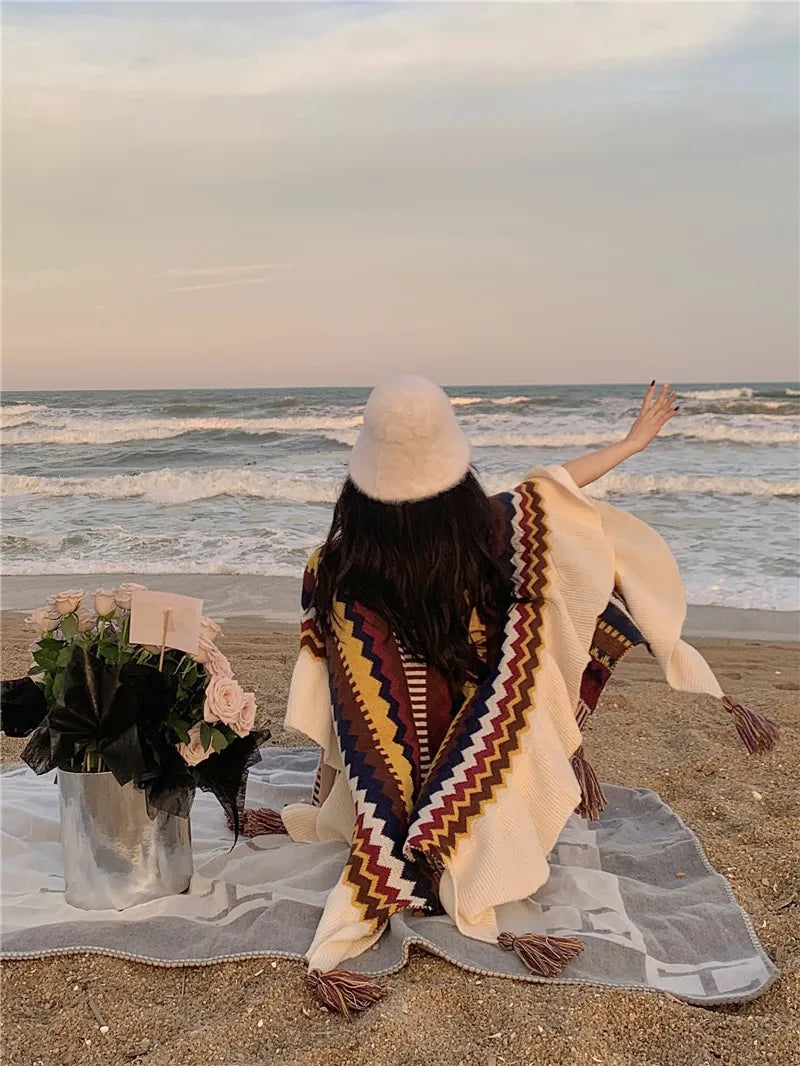 Femme de dos portant le poncho bohème à franges sur une plage, style décontracté et hivernal.