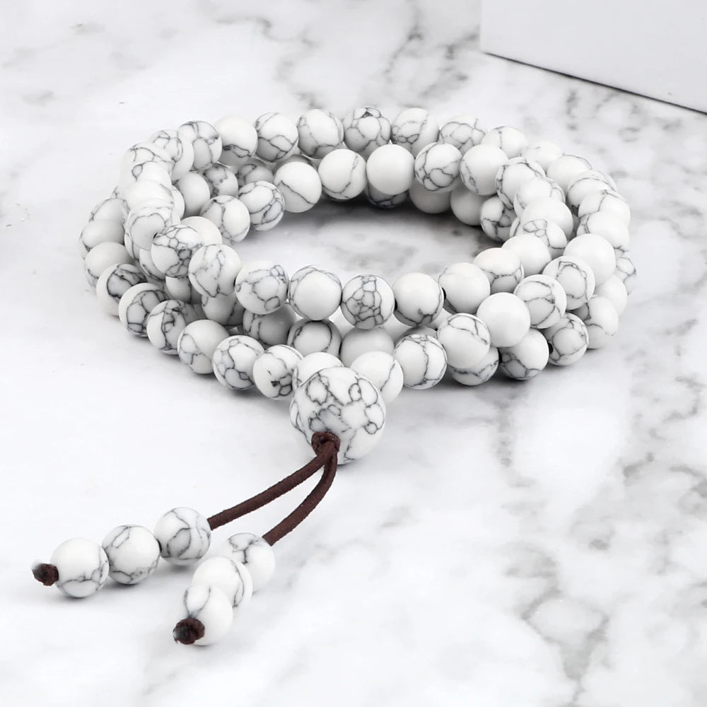 Bracelet mala multi-tours en howlite blanche marbrée, posé à plat sur une surface en marbre.