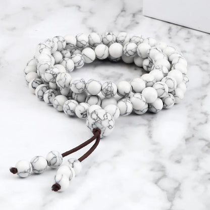 Bracelet mala multi-tours en howlite blanche marbrée, posé à plat sur une surface en marbre.