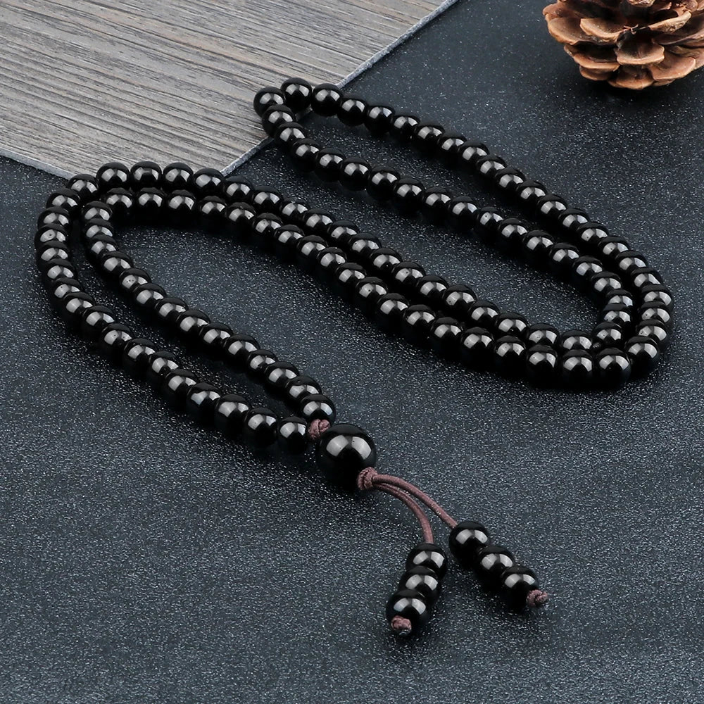 Collier mala 108 perles en pierre naturelle noire disposé sur une surface texturée sombre.