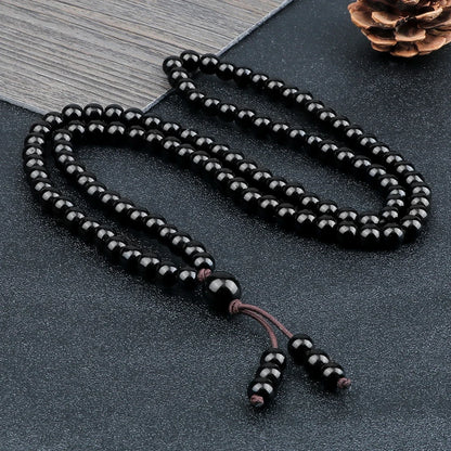 Collier mala 108 perles en pierre naturelle noire disposé sur une surface texturée sombre.