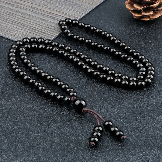 Collier mala 108 perles en pierre naturelle noire disposé sur une surface texturée sombre.