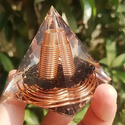 Pyramide orgonite en résine tenue en main, révélant une spirale de cuivre et des éclats d'obsidienne noire.