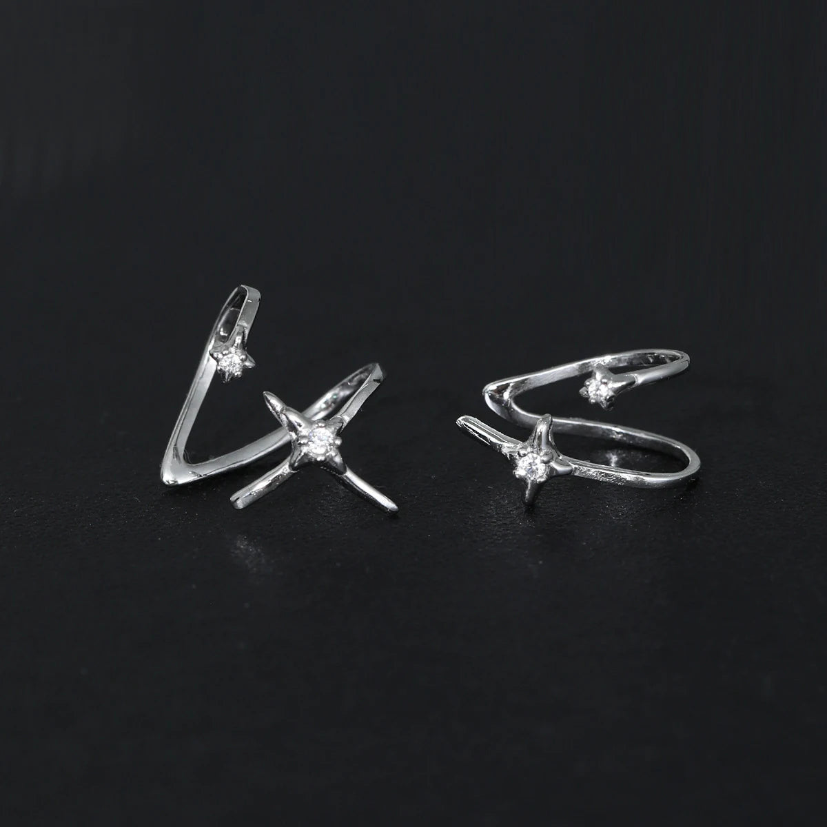 Paire de bagues d'oreille en argent 925 avec étoiles et zircons posées sur un fond noir texturé.
