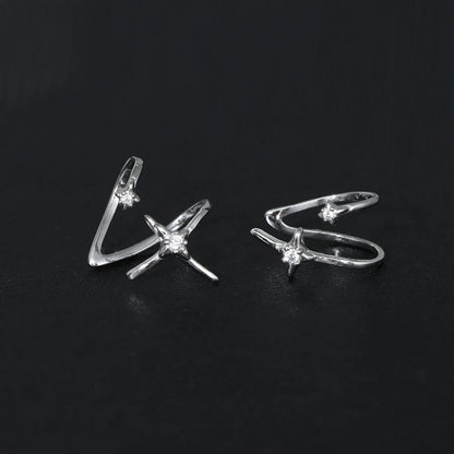 Paire de bagues d'oreille en argent 925 avec étoiles et zircons posées sur un fond noir texturé.