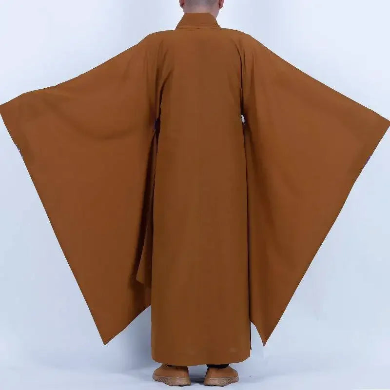 Vue arrière d'un pratiquant en robe ocre, bras ouverts montrant l'amplitude des manches.