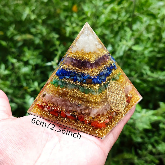 Pyramide orgonite 7 chakras avec mandala fleur de vie doré sur fond de verdure, vue de face.