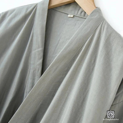 Zoom sur la texture raffinée du tissu d'un kimono gris, soulignant la qualité et la sophistication du vêtement. La douceur du tissu et la teinte neutre offrent une esthétique à la fois simple et élégante.