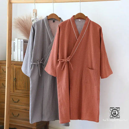 Deux kimonos, l'un gris et l'autre terracotta, élégamment suspendus côte à côte sur un cintre en bois, démontrant un contraste de couleurs harmonieux.