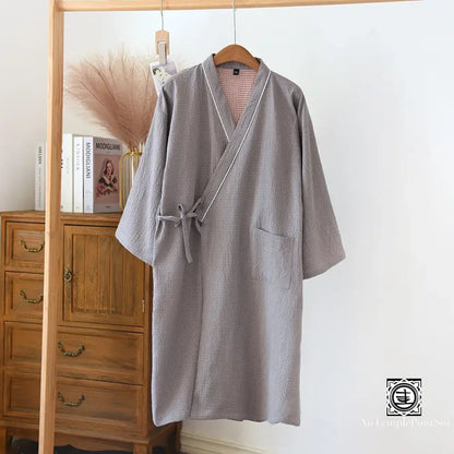 Kimono gris suspendu sur un cintre en bois avec une texture waffle, évoquant confort et simplicité.