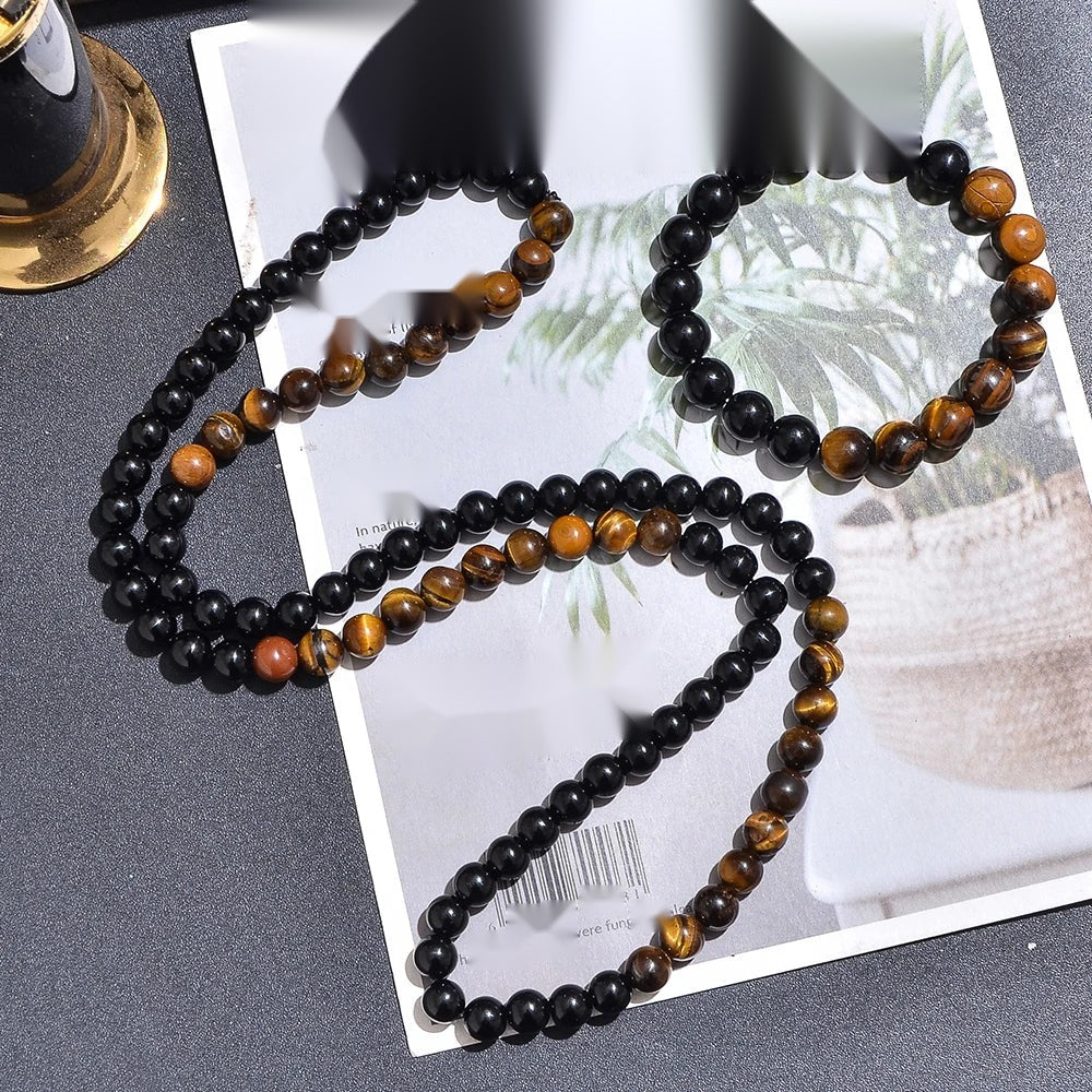 Collier long et bracelet assorti en perles d'œil de tigre jaune et onyx noir posés sur un magazine.