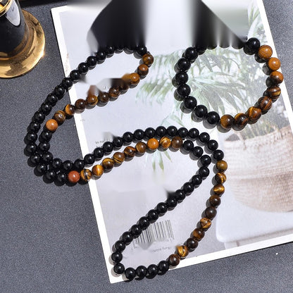 Collier long et bracelet assorti en perles d'œil de tigre jaune et onyx noir posés sur un magazine.